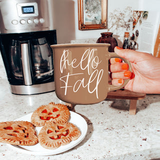 hello fall mug next to stack of sweaters
hello fall coffee cup on kitchen island
hello fall mug on round wooden riser
hello fall mug with neutral fall tablescape